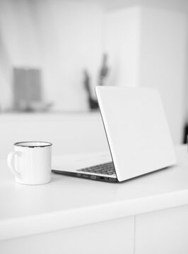 black and white image of a white working laptop at the table next to a white cup. work online