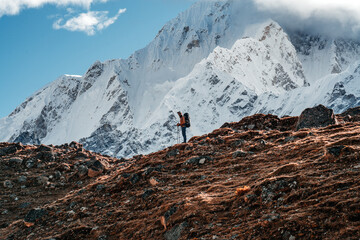 Solo hiker exploring high altitude sunny mountains. Outdoor tourist wearing mountain equipment walking across huge massive rocky way