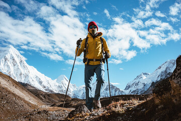 Professional expeditor with trekking sticks and traveling backpack going by mountains tack. Solo tourist hiking across high snowy mountain