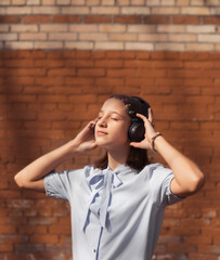 A young teenage girl wearing headphones is outside on a sunny day. The concept of joy and relaxation.