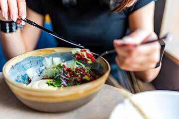 Young woman hand eating beef tartare using knife and fork fom bowl in cafe