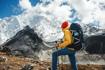 Solo tourist with travel backpack stand in front of snowy and cloudy mountains. Traveler among high...