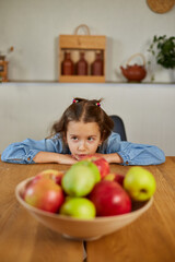 Fototapeta na wymiar Little sad girl look on bowl with fruits in the kitchen at home