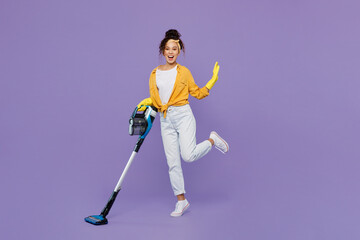 Full body side view fun young housekeeper woman wearing yellow shirt rubber gloves use vacuum...
