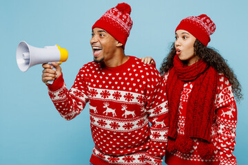Side view merry young couple two man woman in red Christmas sweater Santa hat posing hold scream...