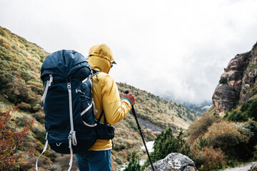 Young hiker traveling across hazy mountain. Man tourist walk by foggy rocky track wearing backpack