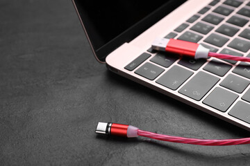Red USB cable with type C connector and laptop on black slate table, closeup