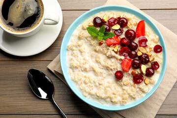 Bowl of oatmeal porridge served with berries on wooden table, flat lay