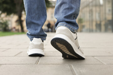 Man in jeans and sneakers walking on city street, closeup