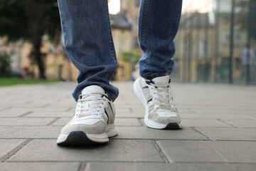 Fototapeta na wymiar Man in jeans and sneakers walking on city street, closeup