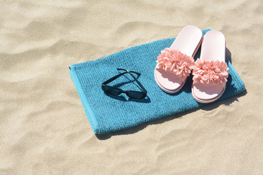 Towel, flip flops and sunglasses on sand. Beach accessories