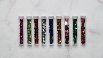 Many colorful sequins in containers on light grey background, top view