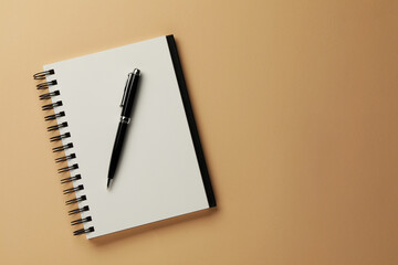 Notebook and pen on beige background, top view. Space for text
