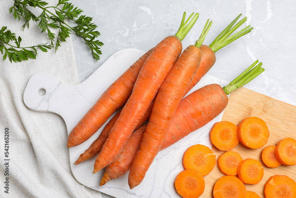 Wall mural whole and sliced fresh ripe juicy carrots on light grey marble table, flat lay