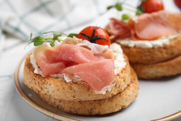 Tasty rusks with prosciutto, cream cheese and tomatoes served on white table, closeup