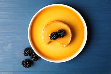 Delicious pudding with caramel and blackberries on blue wooden table, flat lay