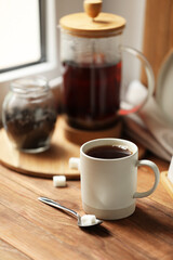 Cup of freshly brewed tea and spoon with sugar on wooden table, space for text