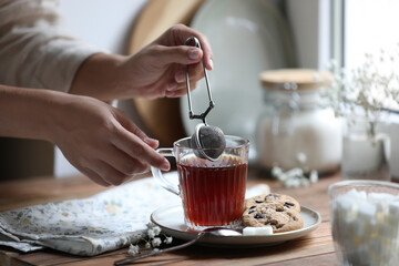 Young woman using snap infuser for brewing tea at wooden table, closeup
