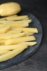 Whole and cut raw potatoes on grey table, closeup. Cooking delicious French fries