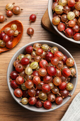 Bowls full of ripe gooseberries on wooden table, above view
