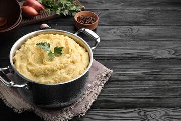 Pot of tasty mashed potatoes with parsley on black wooden table. Space for text