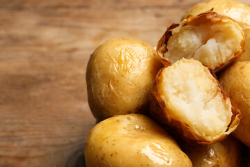 Bowl of tasty whole baked potatoes on wooden table, closeup. Space for text