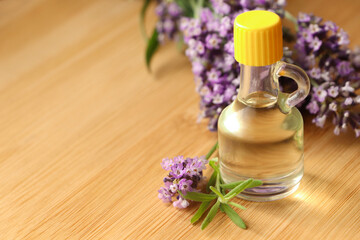 Obraz na płótnie Canvas Bottle of natural essential oil and lavender flowers on wooden table, closeup. Space for text