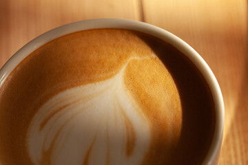 Cup of cappuccino on wooden table under morning light. Close up