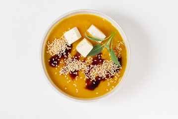 Pumpkin soup puree with sauce, sage leaves, cheese and sesame seeds in a white bowl isolated top view