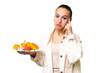 Young Arab woman holding waffles over isolated background thinking an idea