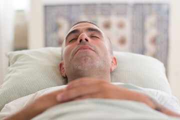Peaceful man sleeping in bed on back with arms on his breast. Medium shot of handsome Caucasian man...