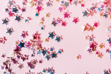 Multicolor holographic Stars Glitter Confetti on pink background. Festive backdrop, selective focus