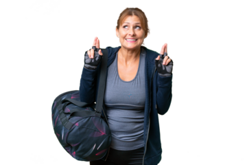 Middle-aged sport woman with sport bag over isolated background with fingers crossing