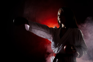 beautiful girl exercising karate punch against red fog background..