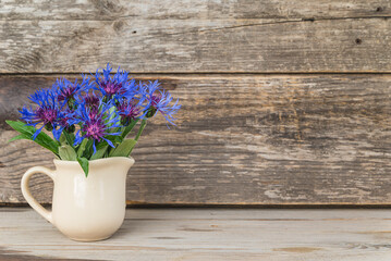 Bouquet of blue cornflowers in jug on old non paint rustic wooden background; copy space