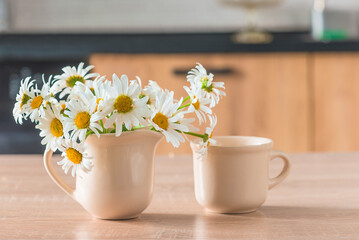 Summer breakfast: cup of coffee and bouquet of white daisies on the table in the kitchen on sunlight