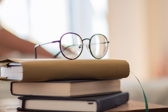 Pile Of Book And Eyeglasses On Bedside Table. Close-up Shot Of Stack Of Hardcover Books For Morning Or Evening Reading. Interior, Education, Development Concept