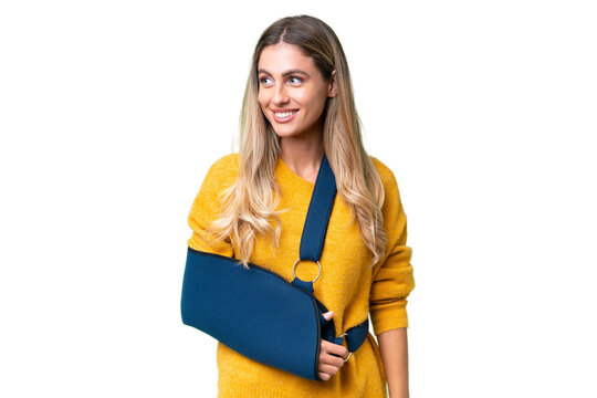 Young Uruguayan woman with broken arm and wearing a sling over isolated background looking side