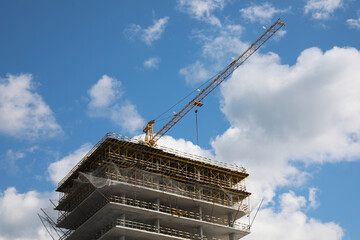 Construction site with tower crane on unfinished building under blue cloudy sky