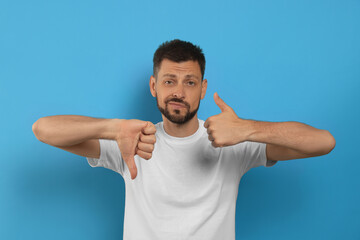 Fototapeta premium Man showing thumbs up and down on light blue background