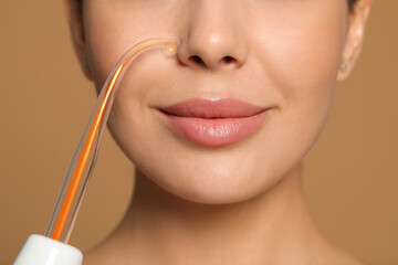 Woman using high frequency darsonval device on beige background, closeup