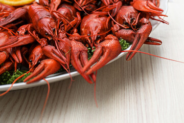 Plate with delicious red boiled crayfish on white wooden table, closeup