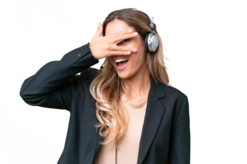 Telemarketer pretty Uruguayan woman working with a headset over isolated background covering eyes by hands and smiling
