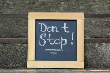 Chalkboard with phrase Don't Stop on stone stairs outdoors