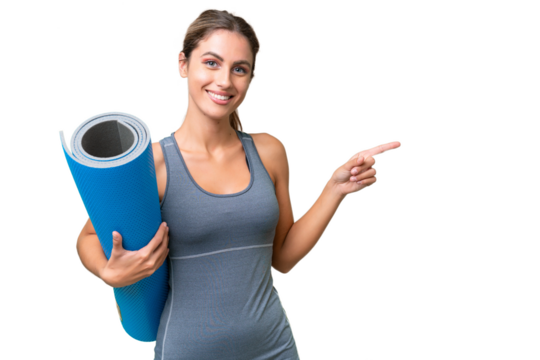 Pretty Young Uruguayan sport woman going to yoga classes while holding a mat over isolated background pointing finger to the side