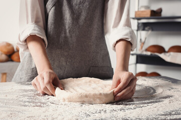 Woman kneading dough at table in kitchen, closeup