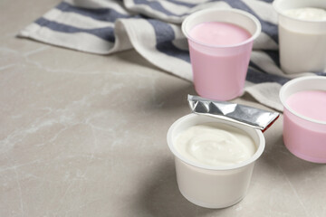 Plastic cups with delicious organic yogurt on grey marble table, space for text