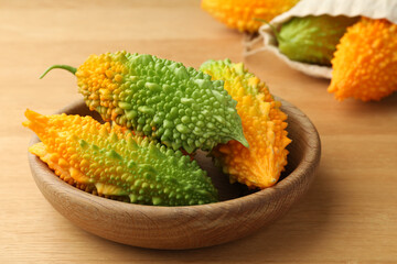 Bowl with fresh bitter melons on wooden table, closeup