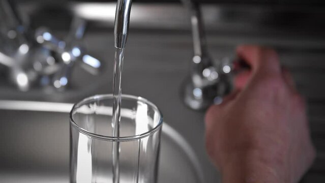 Slow motion shooting of a man pouring a glass of clean, filtered water from a flow filter faucet. Water flows into a glass.