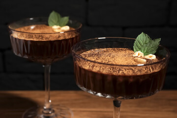 Dessert bowls of delicious hot chocolate with hazelnuts and fresh mint on wooden table, closeup